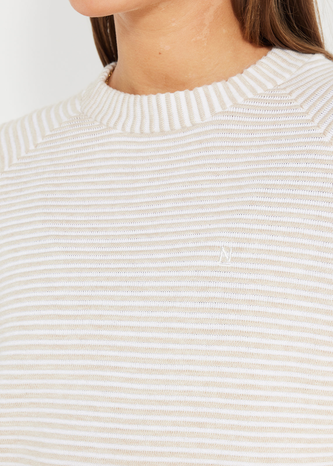 Close-up of beige and white striped knit jumper with embroidered logo detail