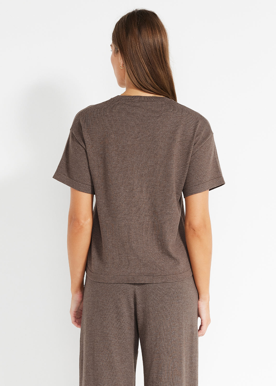 Back view of a woman wearing a relaxed brown knit short-sleeve top with matching wide-leg pants, showing the garment’s soft drape and minimal seam detailing