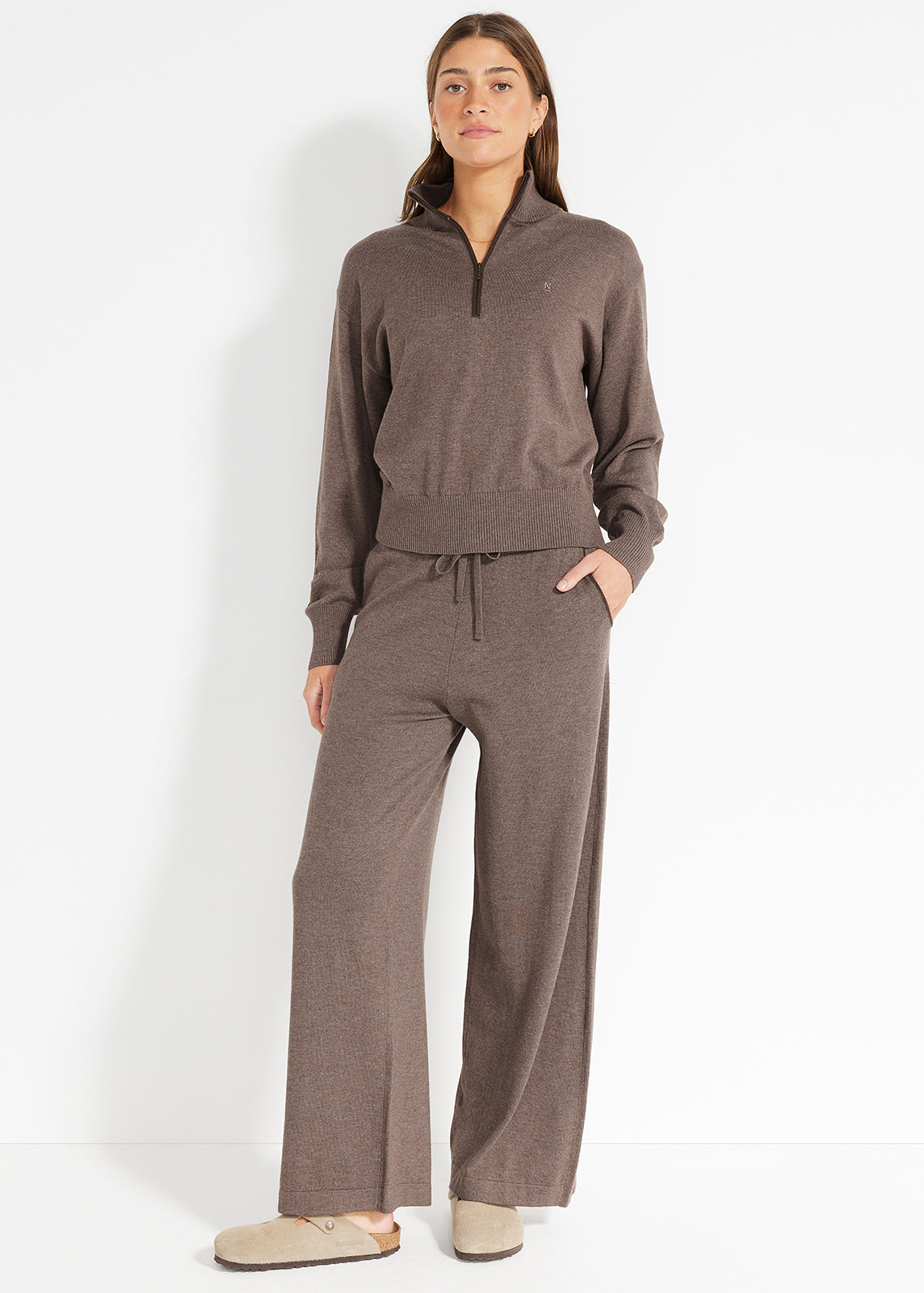 Model wearing brown knit half-zip jumper and matching wide-leg pants styled with slippers