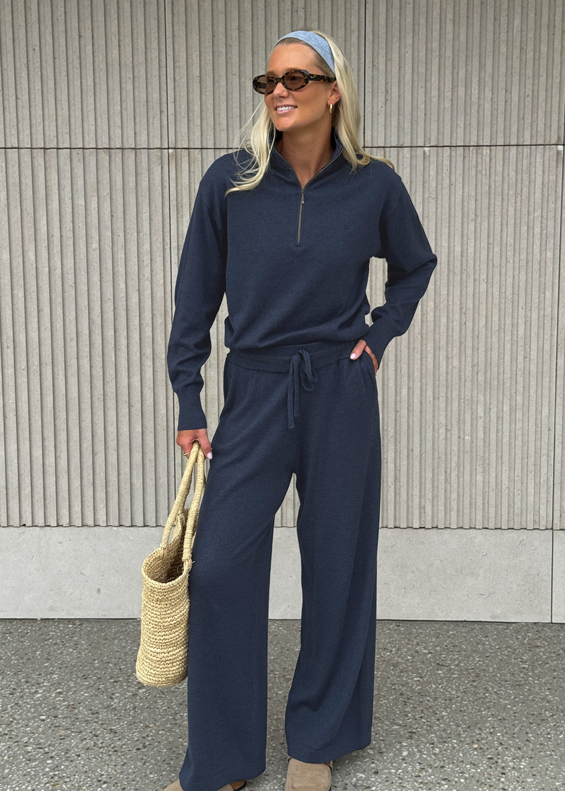 Model wearing navy half-zip knit set styled with headband, sunglasses and woven tote bag
