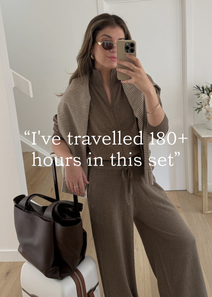 Mirror selfie showing woman wearing brown knit travel set with striped jumper draped over shoulders and brown tote bag