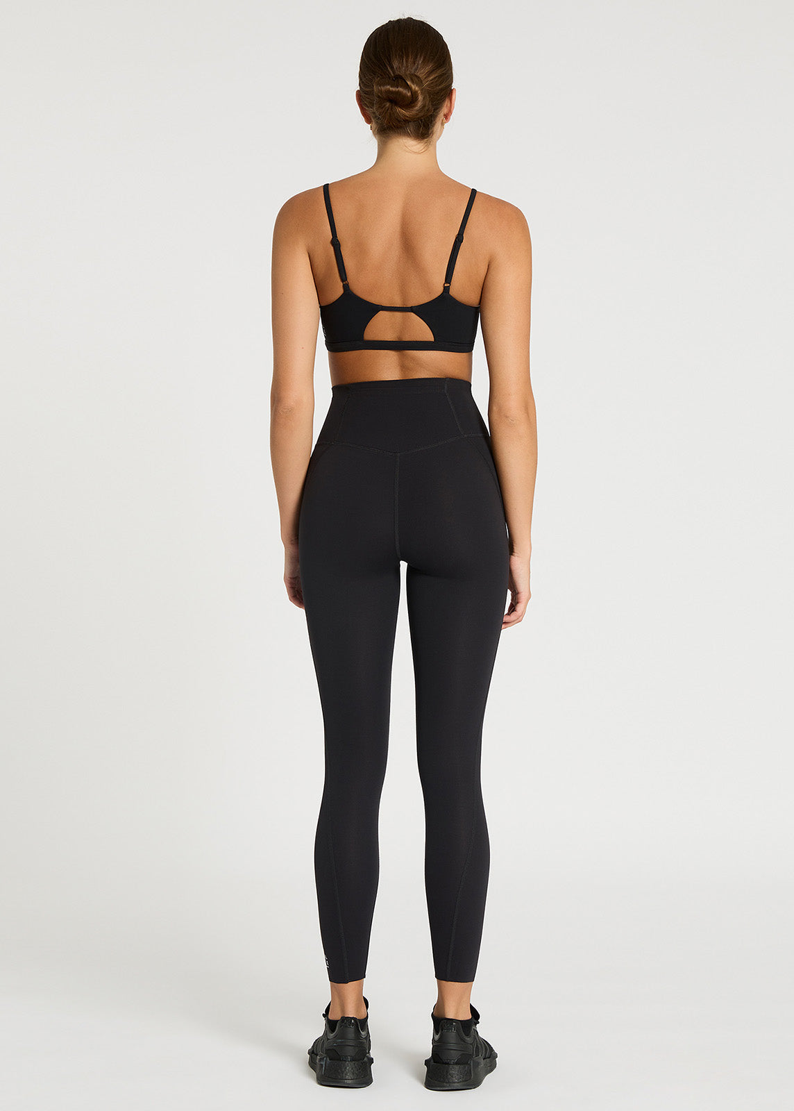Model stood facing backwards wearing black high rise leggings with hidden pocket detail to the back, 7/8 leg length and white logo detail to the bottom of leg.