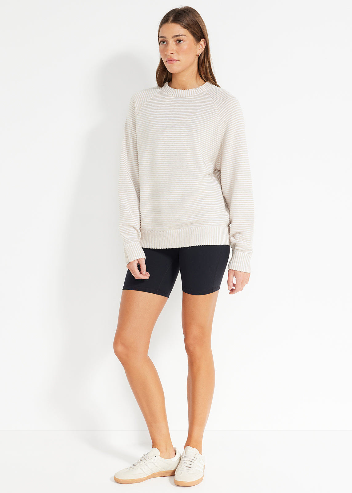 Model wearing striped beige knit jumper with black bike shorts and sneakers