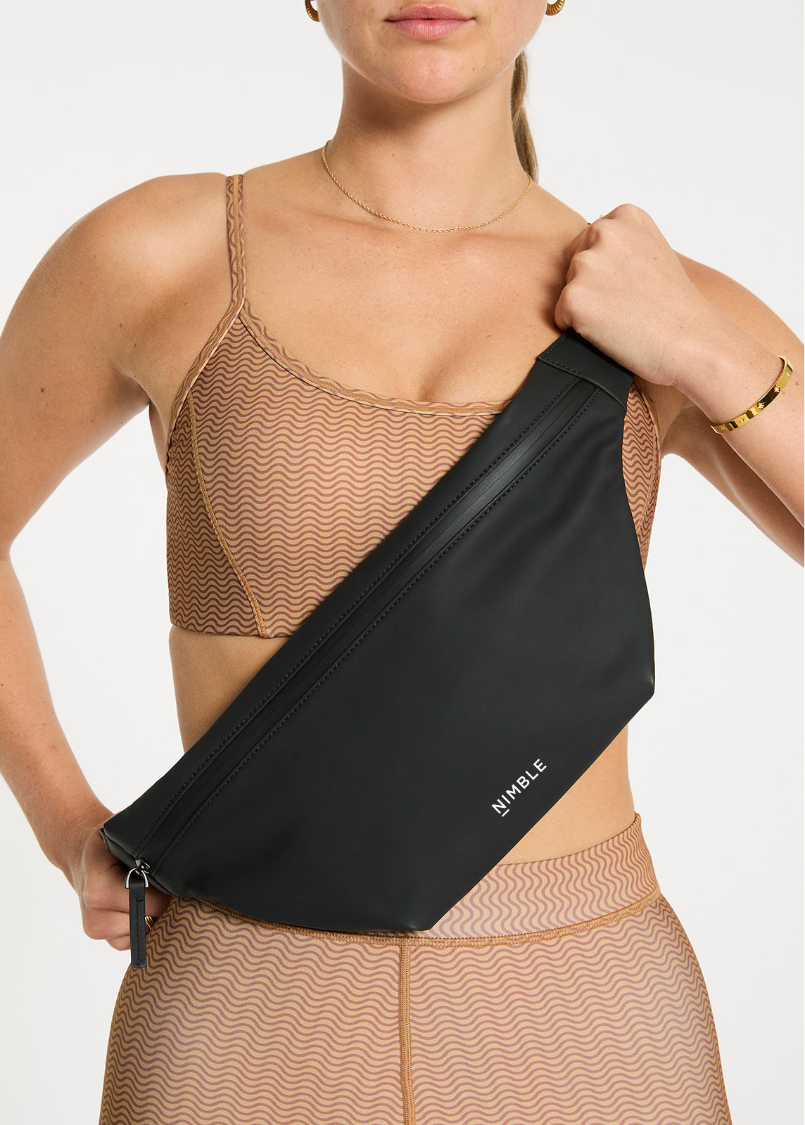 Close Up Of Model Stood Facing Forward Wearing A Black Splash Proof Cross Body Bag With Contrasting White Nimble Logo To The Centre Bottom.