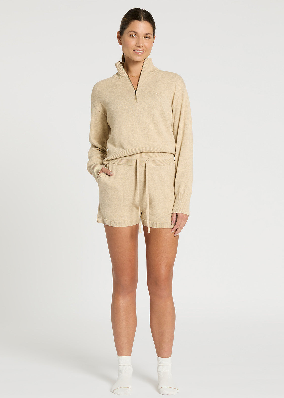 Model stood facing forward wearing oatmeal coloured knit shorts with mid-thigh length, pockets and waistband with drawstring detail with matching knit top tucked in.